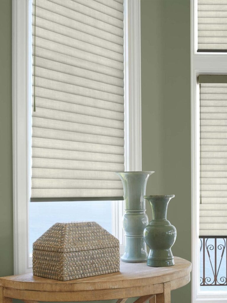 Light-colored fabric window blinds with cord control in a cozy room with green walls and decorative vases.