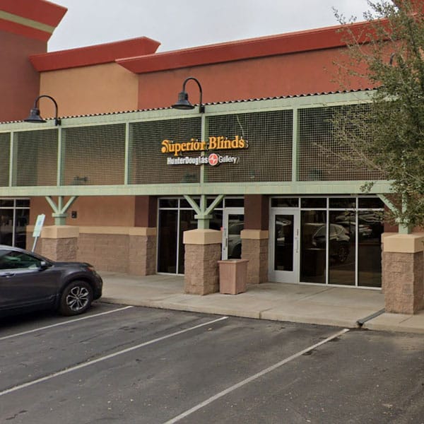 High-quality image of Superior Blinds storefront with a green exterior, showcasing window coverings, in a shopping plaza with parking spaces; ideal for showcasing window treatment showroom.