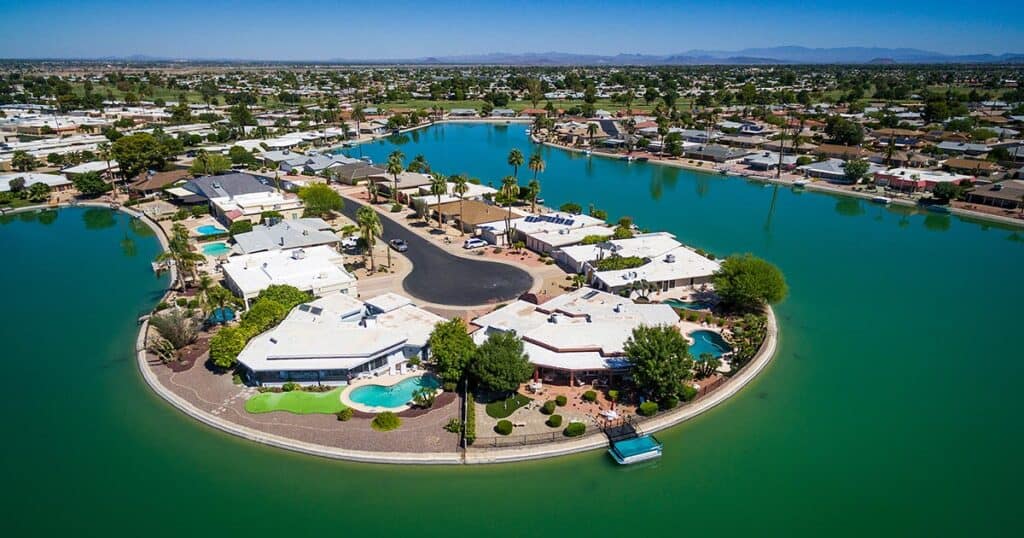 Aerial view of a lakeside residential community with waterfront homes, swimming pools, lush greenery, and a boat dock, showcasing desirable outdoor living spaces and scenic water views.
