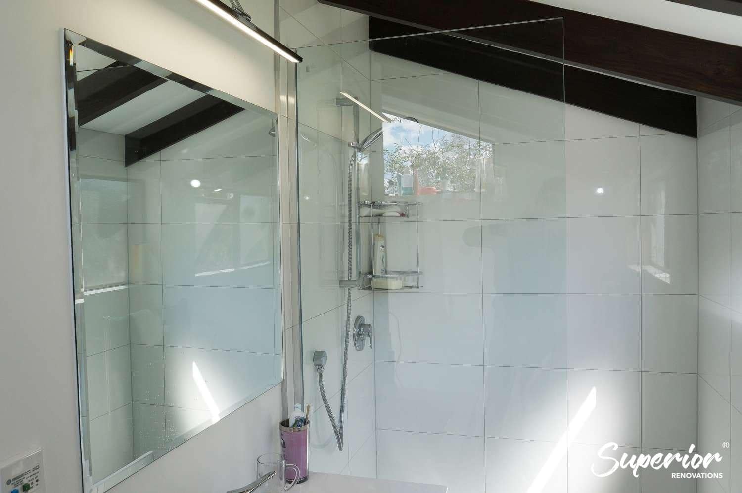 Renovated bathroom with a glass walk-in shower, framed mirror and over-mirror light