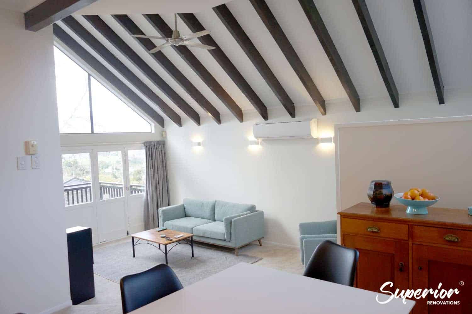 Renovated open-plan living and dining under a raked beamed ceiling with a ceiling fan and a teal sofa