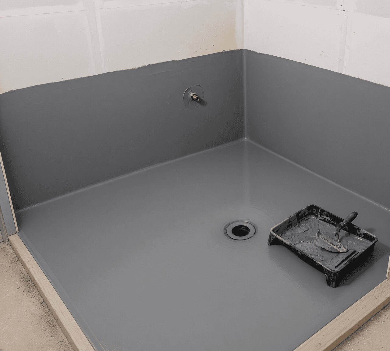 Grey waterproof membrane rolled across a bathroom floor and up the lower walls around the drain and mixer outlet, before tiling