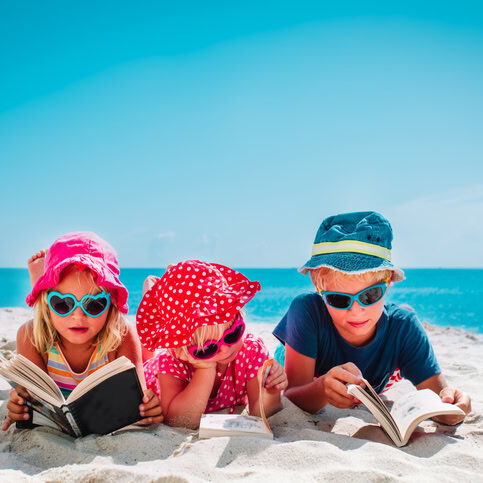 cute happy kids -boy and girls- read books on beach, family vacation concept