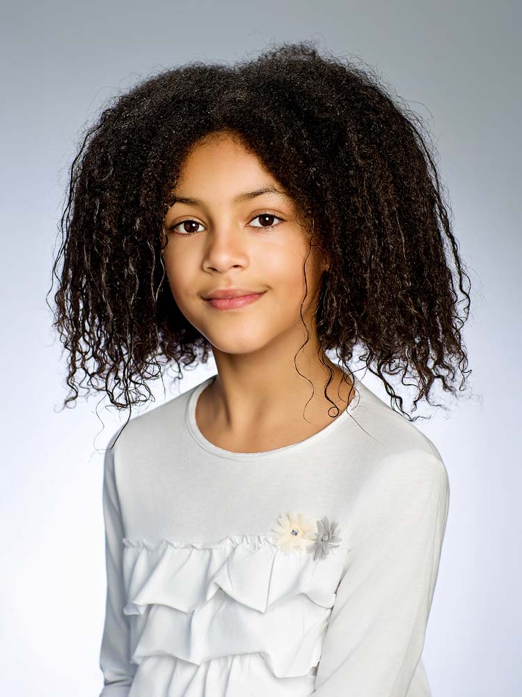Young girl headshot for professional Sussex headshots; natural smile, curly hair, elegant white top, suitable for business or personal branding.