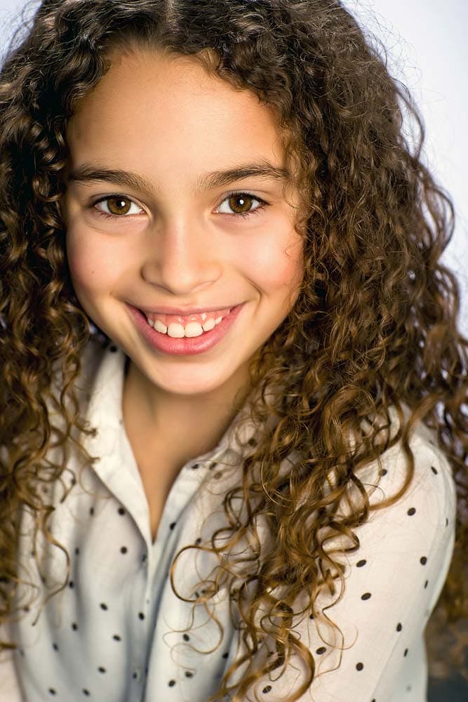 Bright young girl with curly brown hair and cheerful expression, professional headshot for kids, family, or school portraits in Sussex.