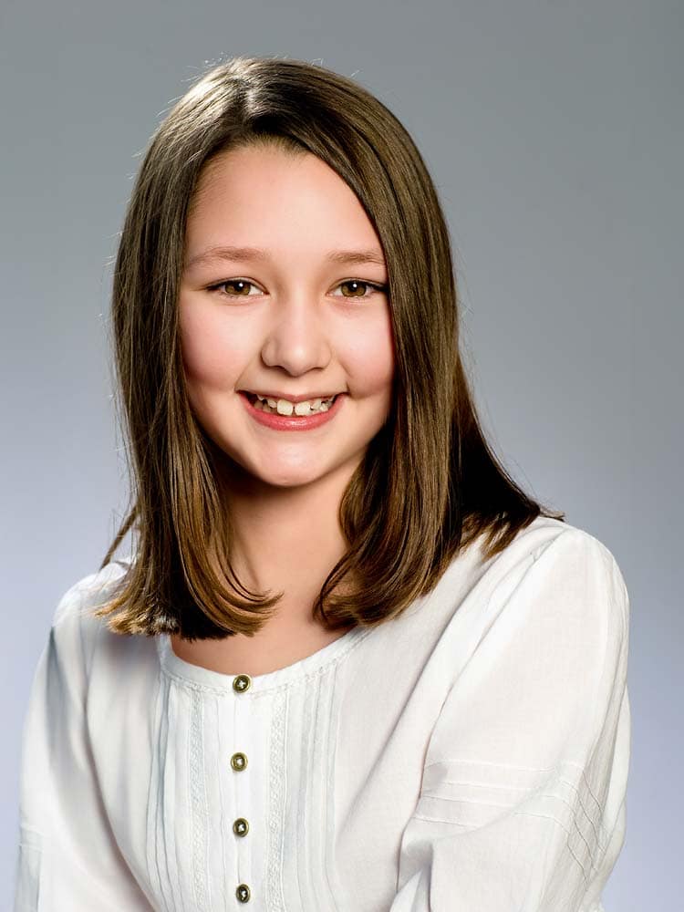Bright smiling young girl with straight brown hair in a white blouse, Sussex headshots for children's portrait photography, professional headshot in Sussex, UK.