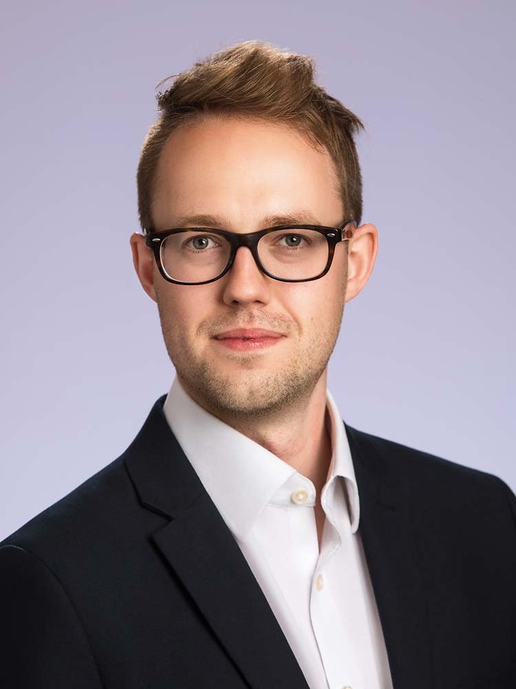 Modern professional headshot of a young man with glasses, wearing a black suit and white shirt, ideal for business profiles, LinkedIn, and corporate branding in Sussex.