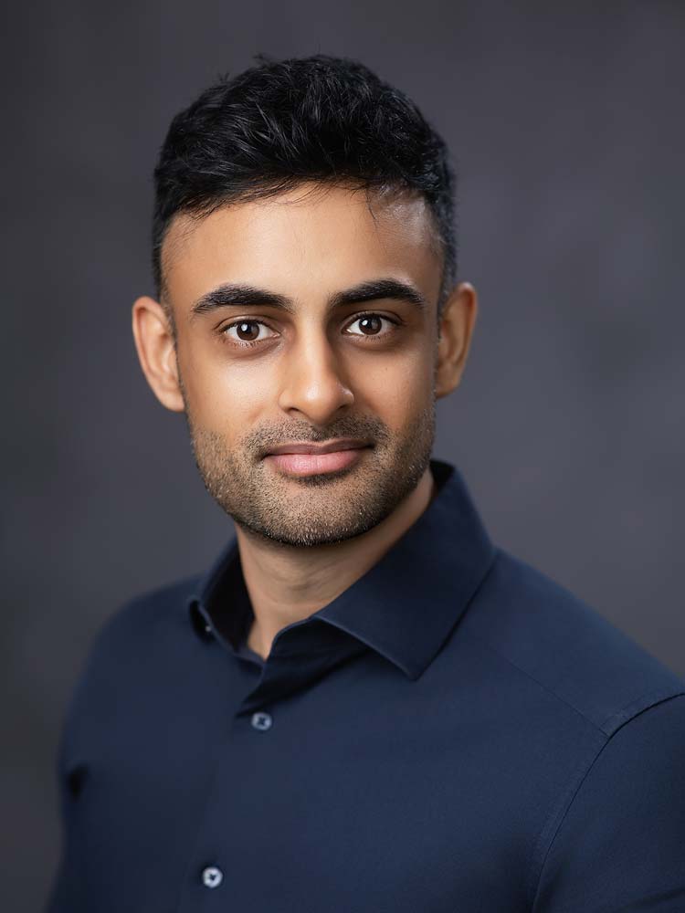 Indian man professional headshot in Sussex, business portrait, high-quality Sussex headshots for corporate or LinkedIn profiles, confident individual in a dark blue shirt against a grey background.