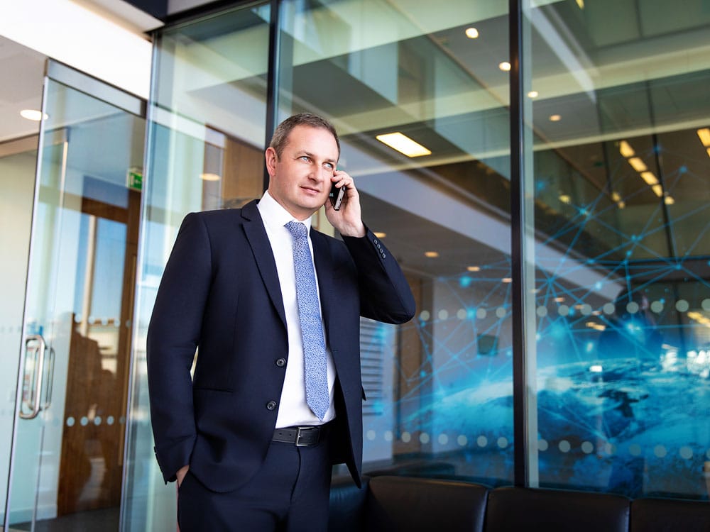 Business professional headshot of a man in a suit talking on mobile phone in modern office setting, Sussex headshots for corporate photography and executive portraits, Sussex Headshots Sussex, UK.