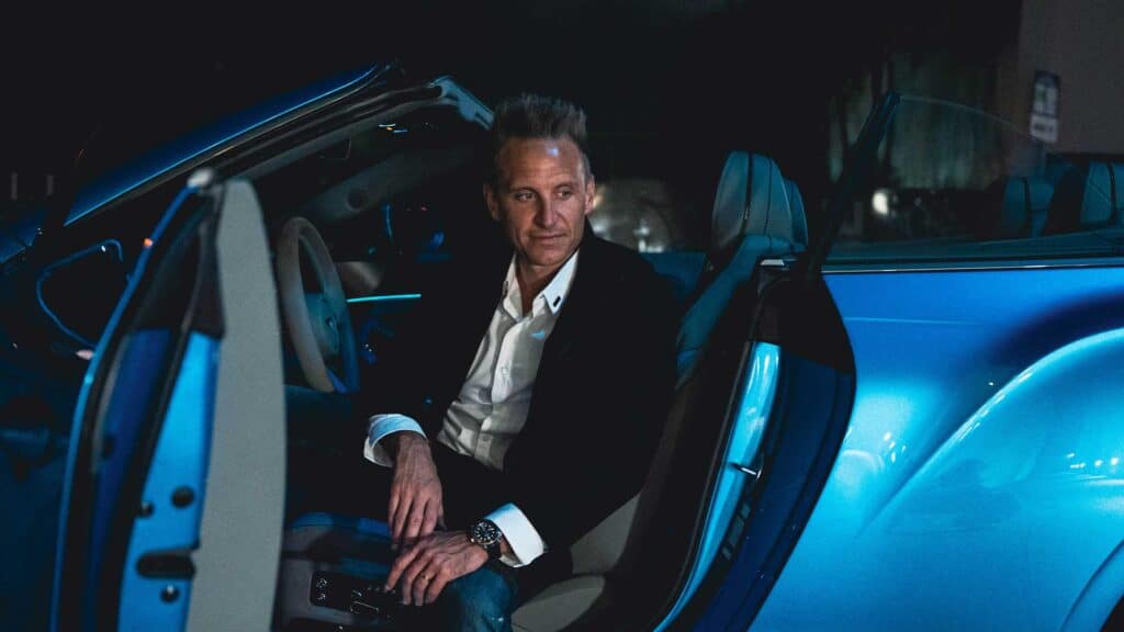 Luxurious man in formal attire sitting inside a modern electric car at night, representing innovation, luxury transportation, and advanced automotive technology.