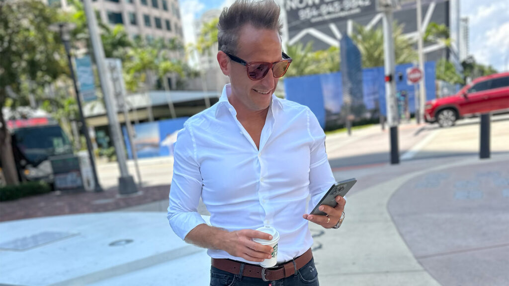 Modern businessman enjoying coffee outdoors while checking his smartphone in an urban setting, showcasing professionalism and connectivity for SEO on business ventures and digital communication.
