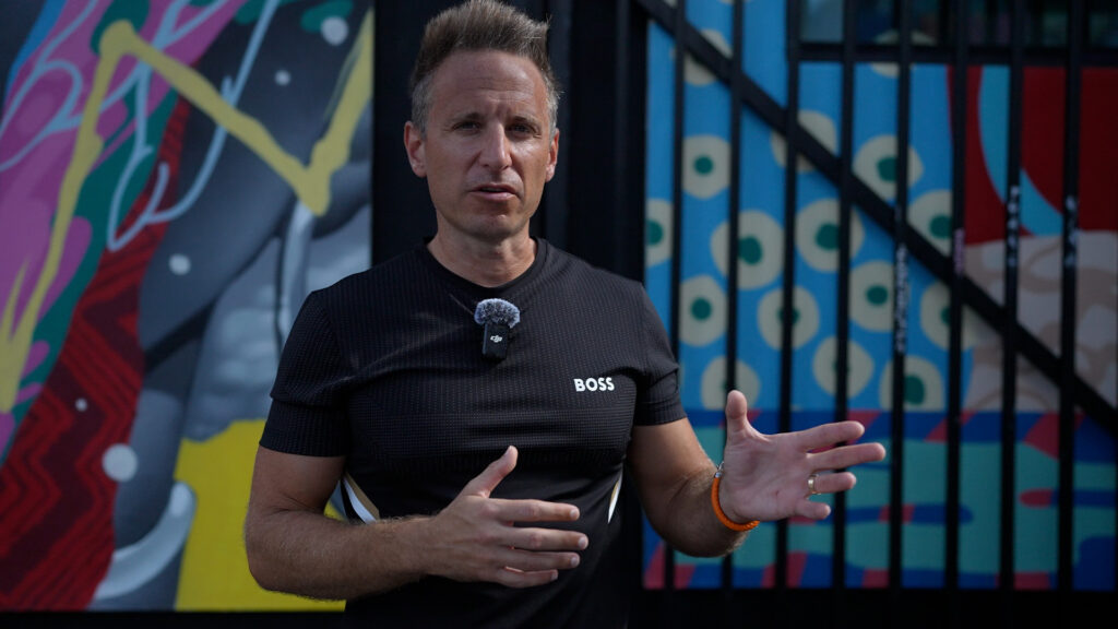 Innovative speaker at an outdoor event featuring colorful graffiti background, emphasizing entrepreneurship, leadership, and motivation for business growth.