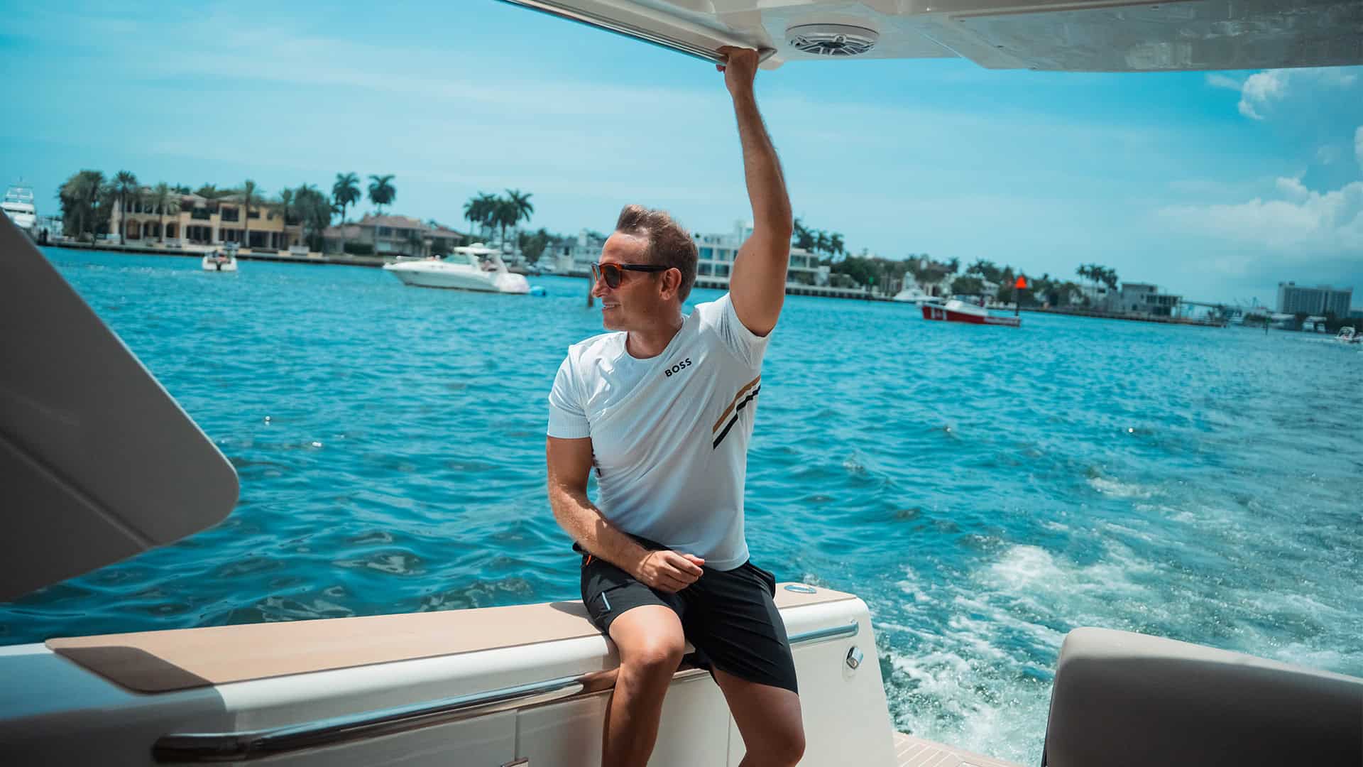 Luxury yacht man enjoying boating experience in Miami waterfront with modern neighbor homes and clear blue sky.