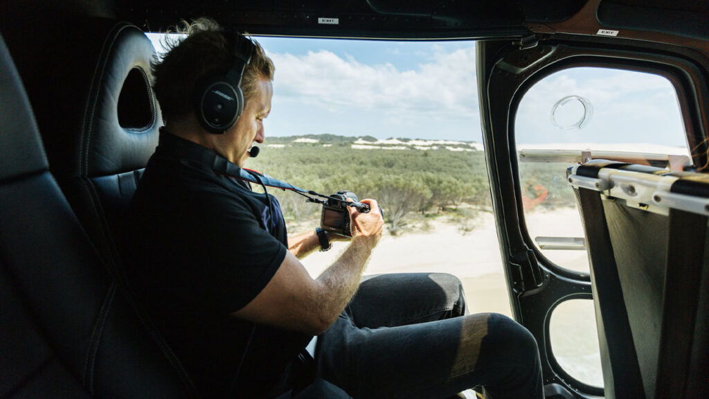 Aerial photographer capturing scenic landscape from helicopter with professional camera, emphasizing adventure, nature photography, and aerial imaging services.