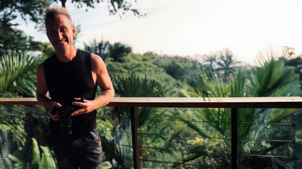 Photographer enjoying nature on a balcony with lush green tropical foliage in the background, capturing moments in a scenic outdoor setting.