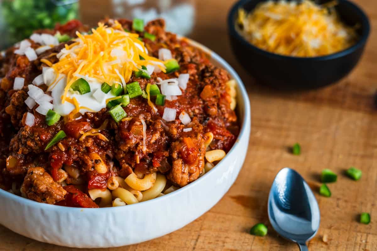 Bowl of Chili Mac topped with sour cream, onion, and jalapenos