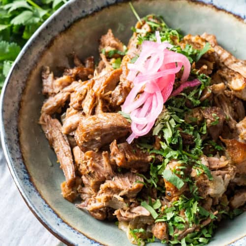 Pork Carnitas in a bowl garnished with cilantro and pickled red onion