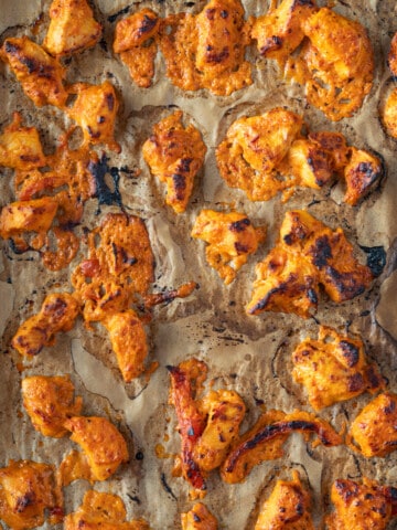 Marinaded and roasted chicken on a sheet tray that is red on color