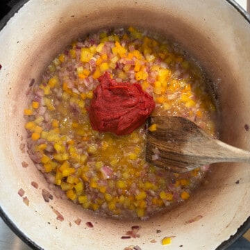 adding tomato paste to peppers and onions in a dutch oven for chili