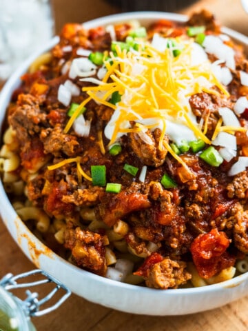 Bowl of chili Mac topped with sour cream and diced onions and jalapenos.