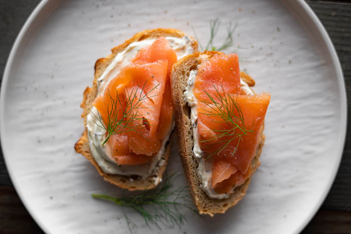Cold-smoked salmon toast garnished with fresh dill on a white plate