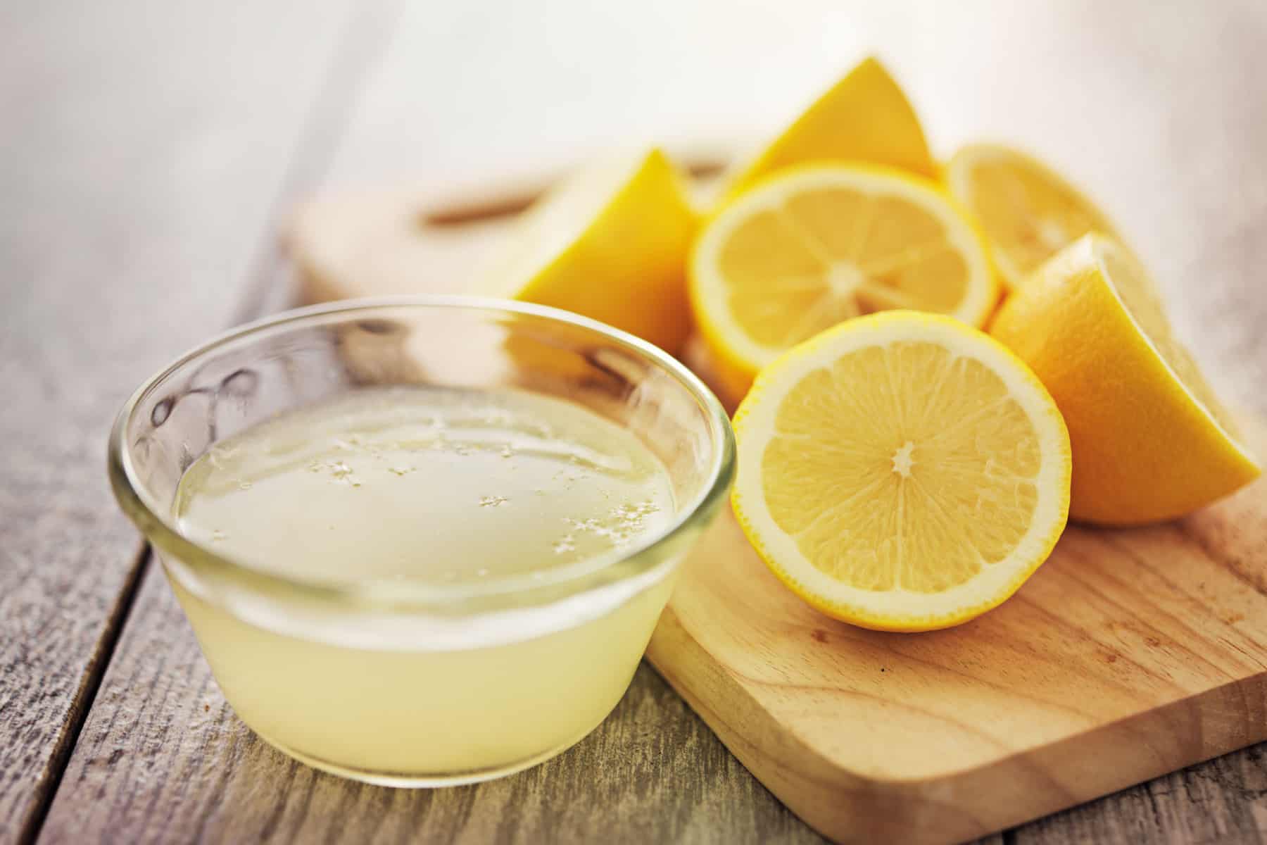 small bowl of lemon juice next to freshly sliced lemons
