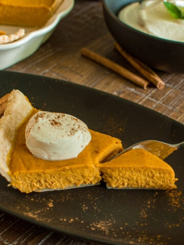 Slice of Pumpkin Pie with whipped cream and a fork cutting into it