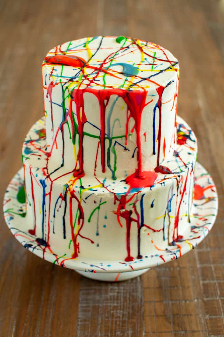 Paint splatter birthday cake with red, blue, yellow, and green splatters on white buttercream