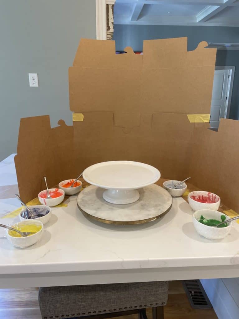 Cake decorating station with cardboard backstop and parchment to catch splatter paint