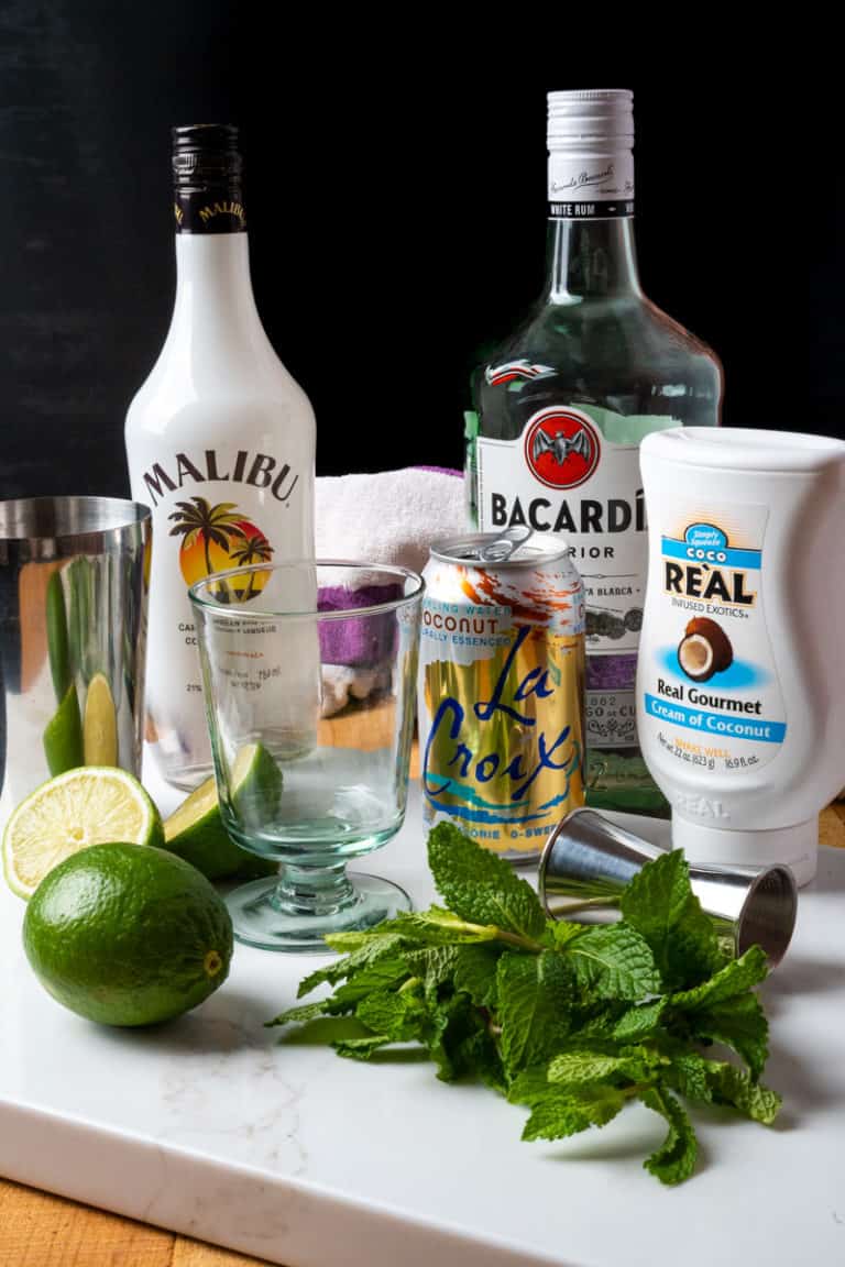 Coconut mojito ingredients flat lay with cream of coconut, white rum, coconut rum, fresh mint, and lime