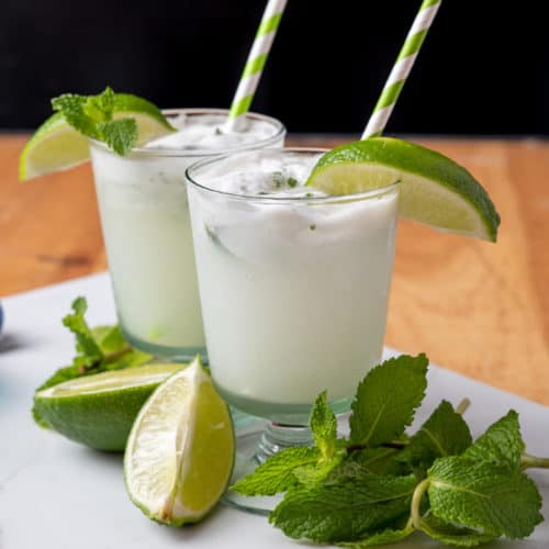 Two creamy coconut mojitos in highball glasses with mint and lime garnish ready to serve