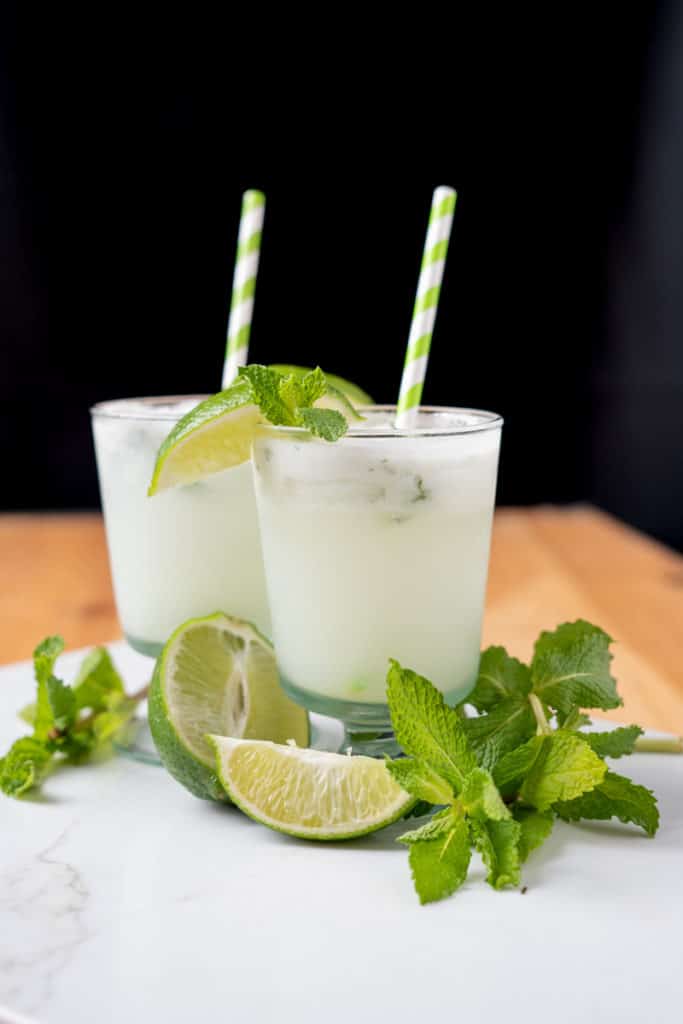 Creamy coconut mojito with green striped paper straws, fresh mint, and lime wedges