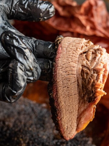 Smoked brisket, sliced, held by a black gloved hand.