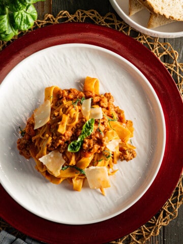Pasta Bolognese on a white plate with a red charger