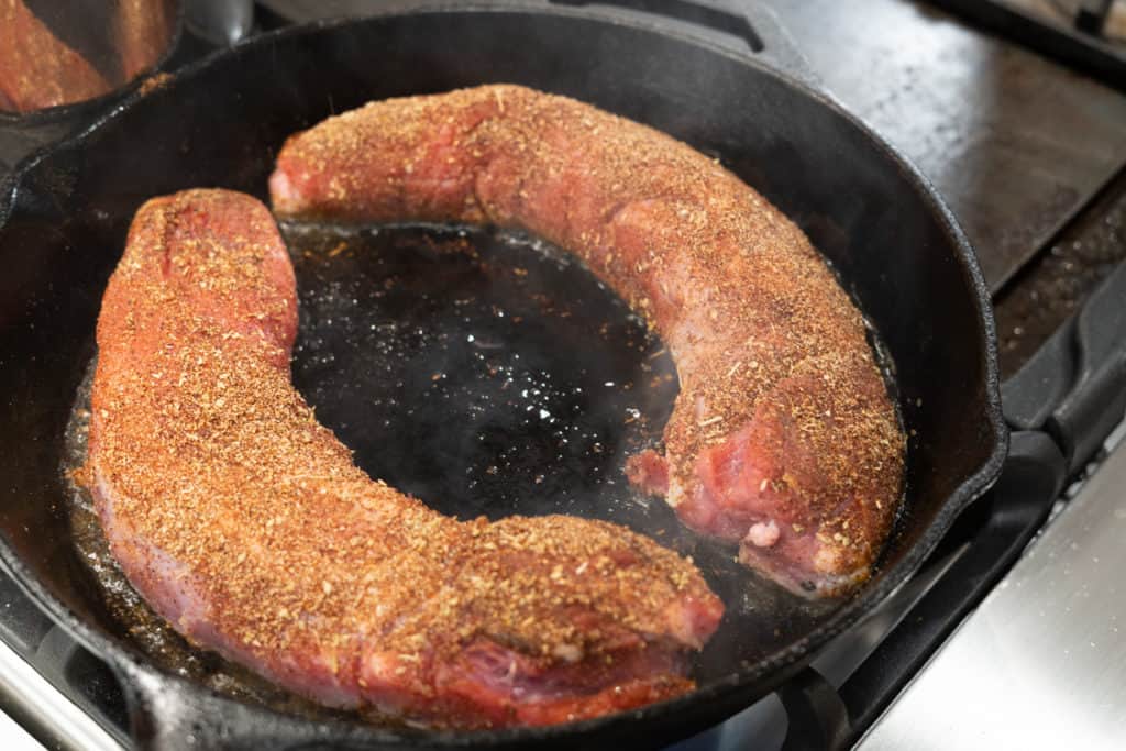 Pork tenderloin searing in a cast iron pan to build a brown crust