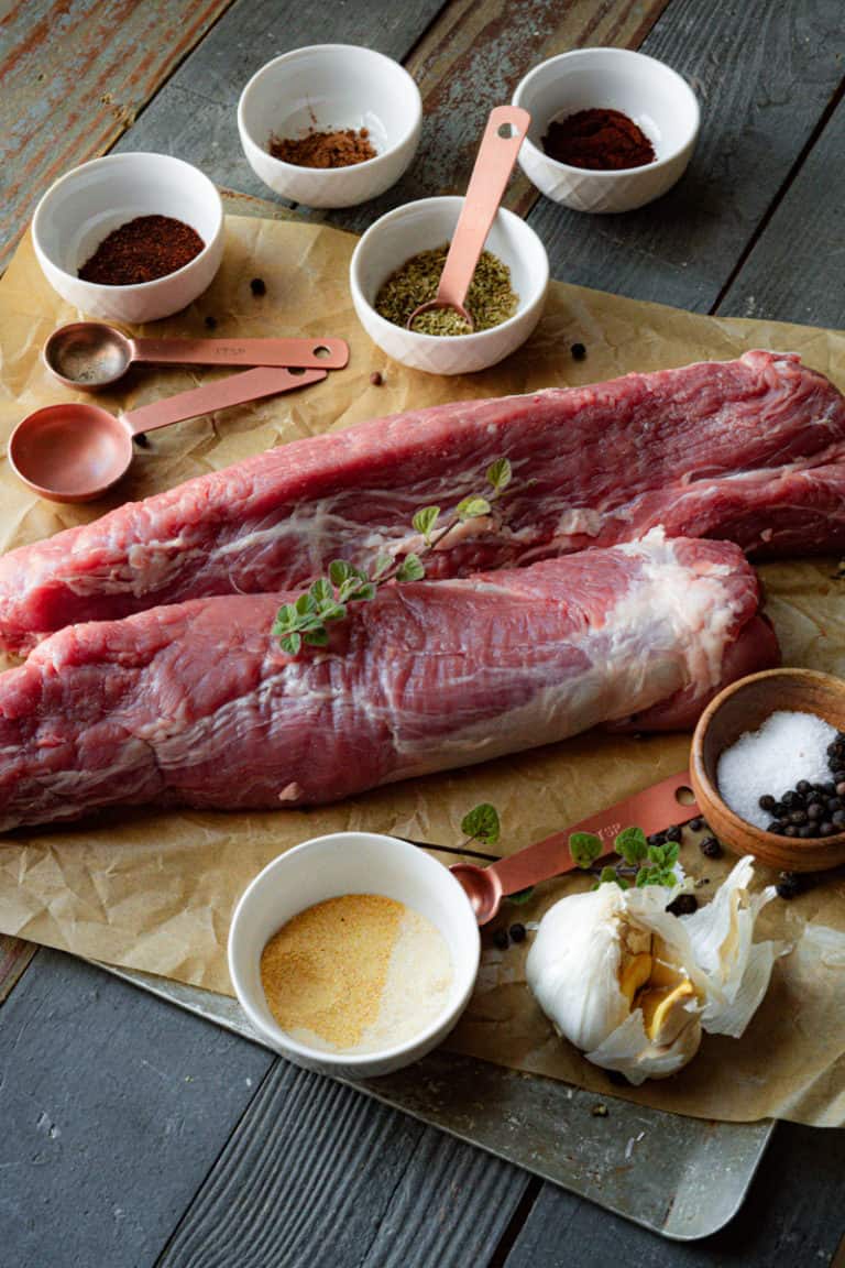Raw pork tenderloin surrounded by chili powder, paprika, and other spice rub ingredients