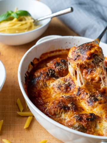 Cheese covered meatball being scooped from a dish