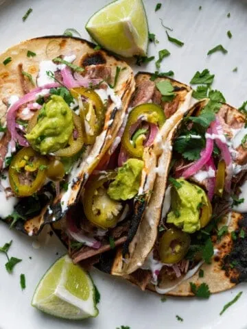 Carnitas street tacos on a white plate garnished with lime and cilantro