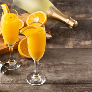 Two orange mimosas with fresh orange slices on a rustic table.