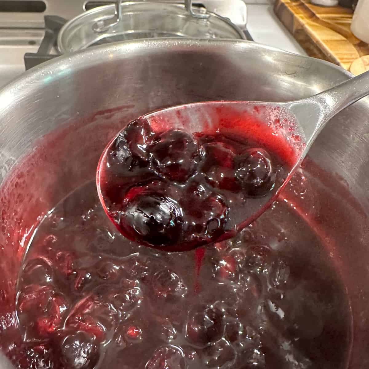 Blueberry compote on a metal spoon being scooped from a pot