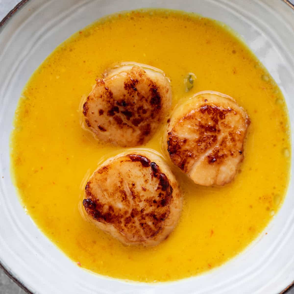 three seared scallops sitting in a yellow bisque