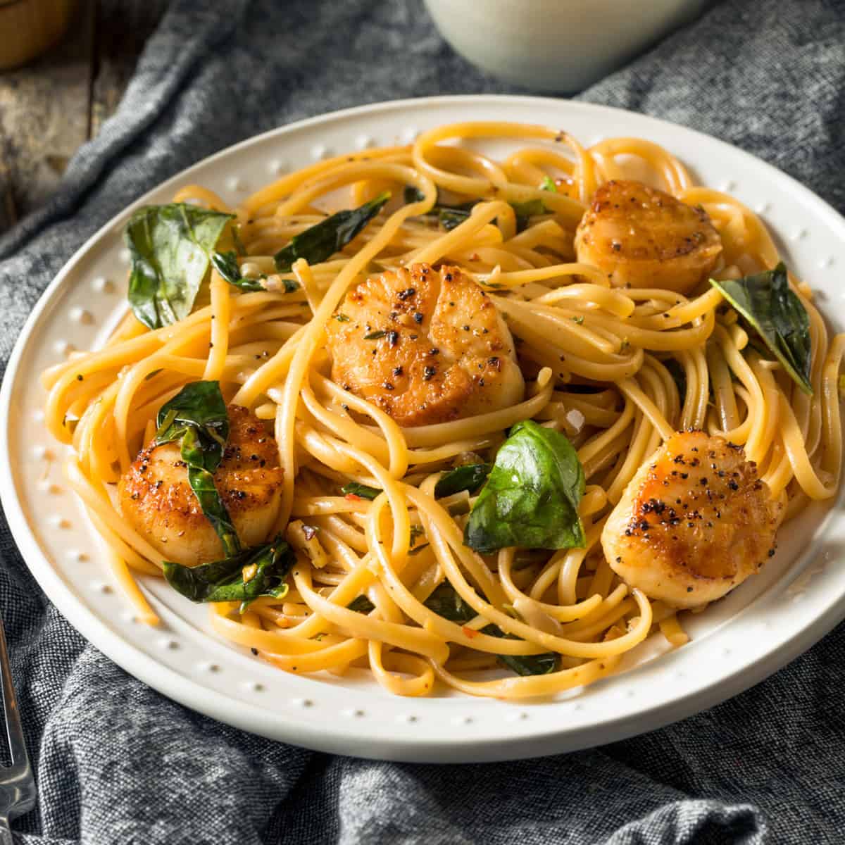 Seared scallops sitting on top of a lightly dressed pasta with fresh basil