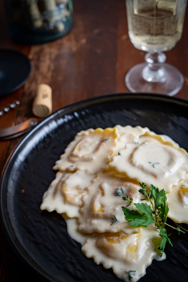ravioli in a cream sauce garnished with fresh time on a black plate