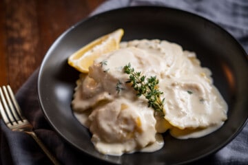 Lobster Ravioli in a cream sauce garnished with fresh thyme in a black bowl