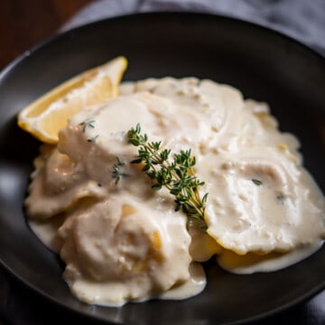 Lobster Ravioli in a cream sauce garnished with fresh thyme in a black bowl