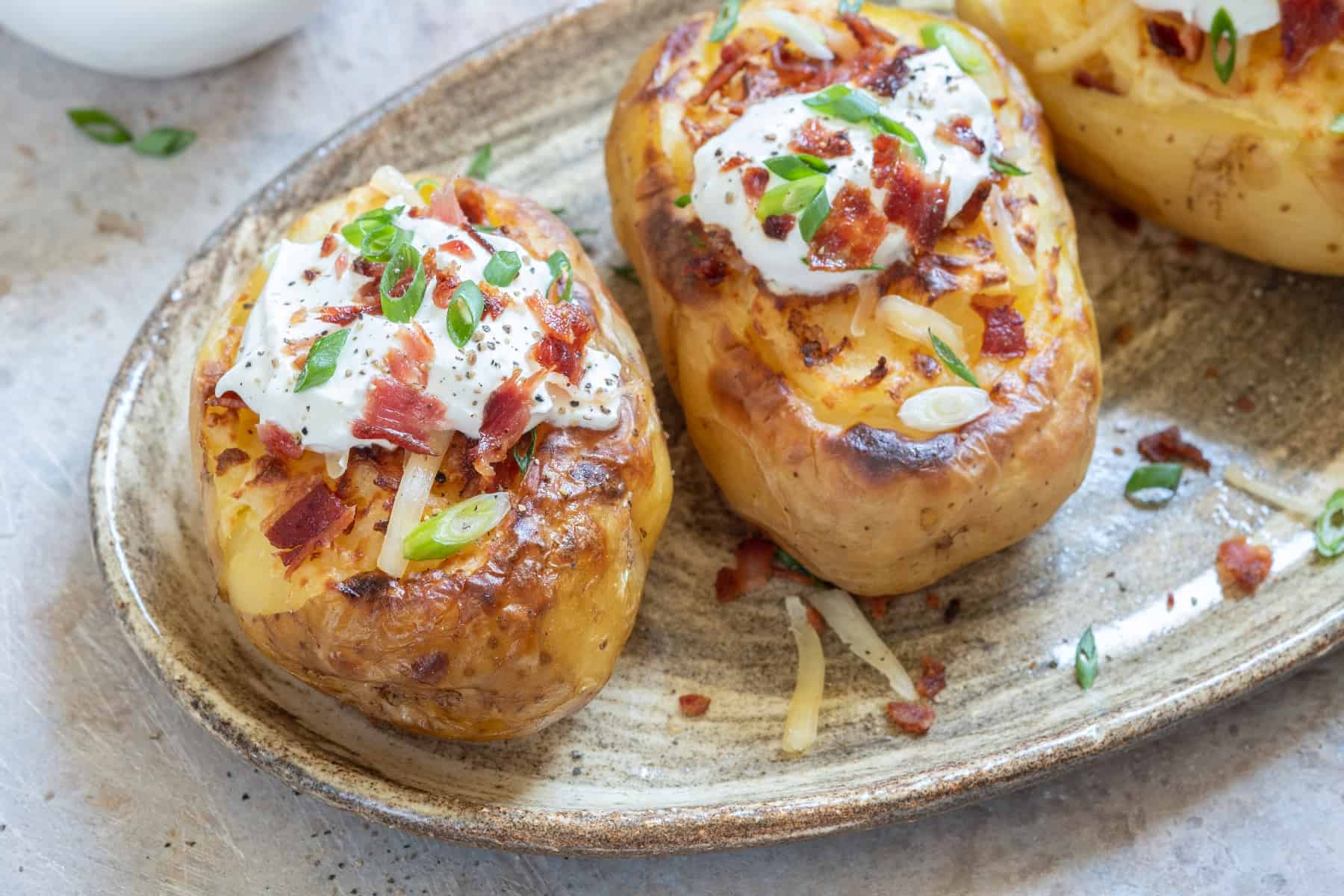 loaded baked potato with sour cream, bacon bits, and green onions on top