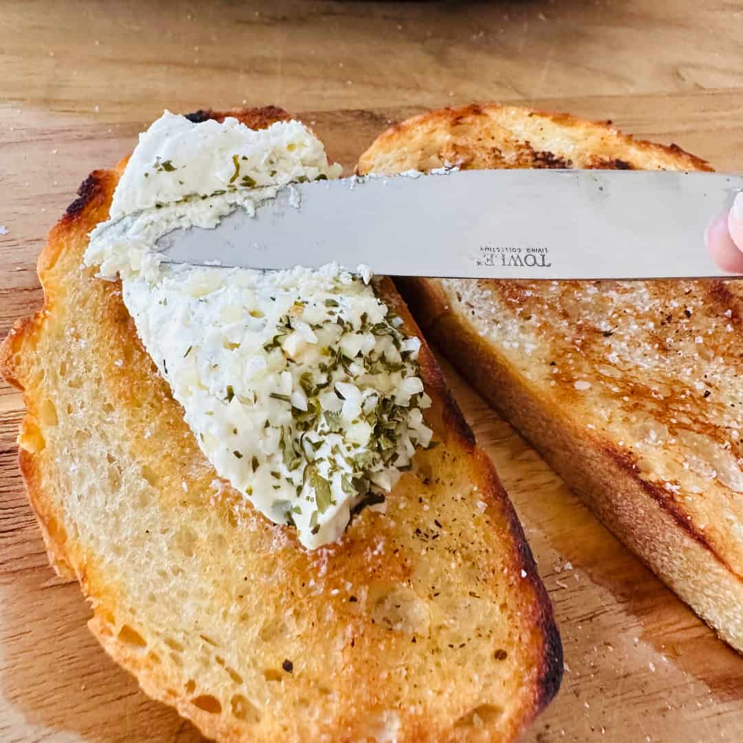 Spreading garlic-herb Alouette cheese on toasted sourdough