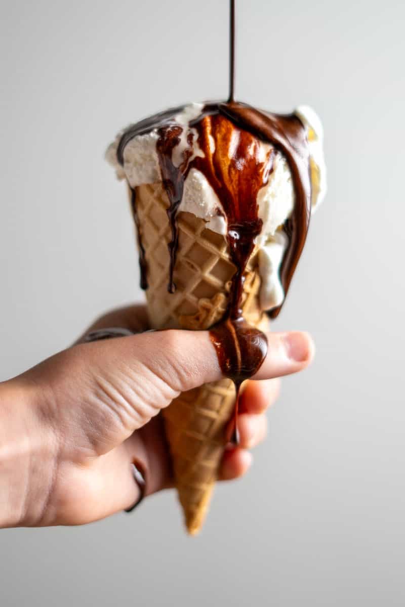 pouring chocolate syrup on a vanilla ice cream cone
