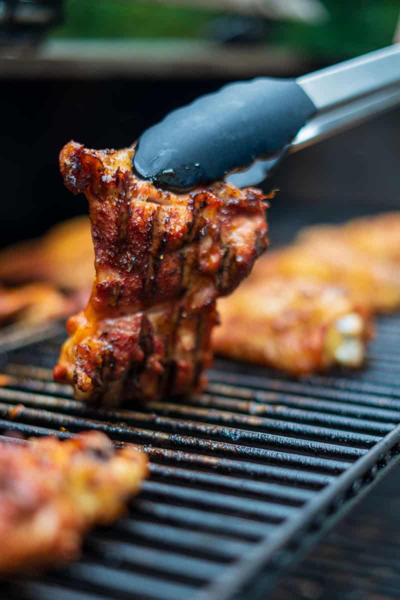 Smoked chicken thighs on a smoker being flipped over with tongs