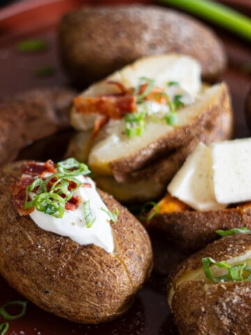 Close-up of smoked baked potatoes topped with cheese, bacon, and green onions.